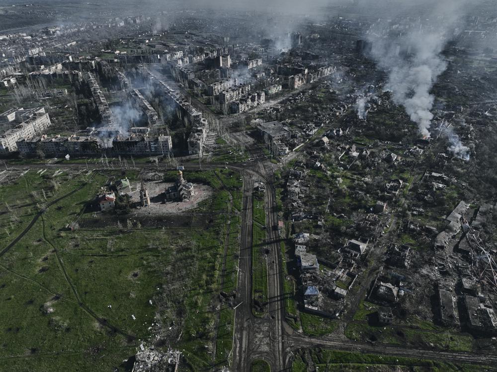 An aerial photo depicting a city engulfed in flames.
                Smoke pillars rise from ruined apartment complexes often missing large parts of the
                building. A landscape cowered in artilery crates.