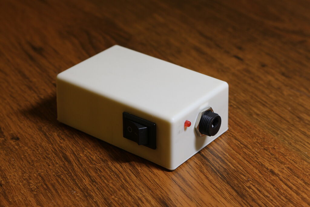 A creme white case with a red LED, barrel jack and on/off switch mounted to it